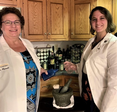 Diane and Lauren Reist, mother and daughter, stand in the kitchen near a mortar and pestle in white coats